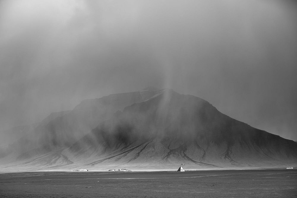 This grey image looks like the moon but instead, it is mist and rain falling on a massive mountain with tiny buildings…