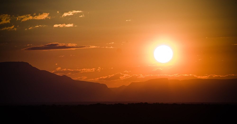The powerful African sun casts glowing orange light across the sky as it sets over a mountain range.