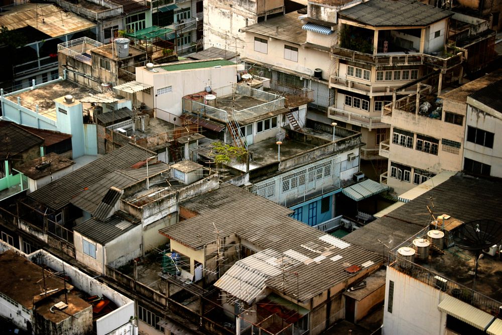 Shot from up in the sky, we are looking down at residential rooftops in Thailand of many different heights, lengths and…