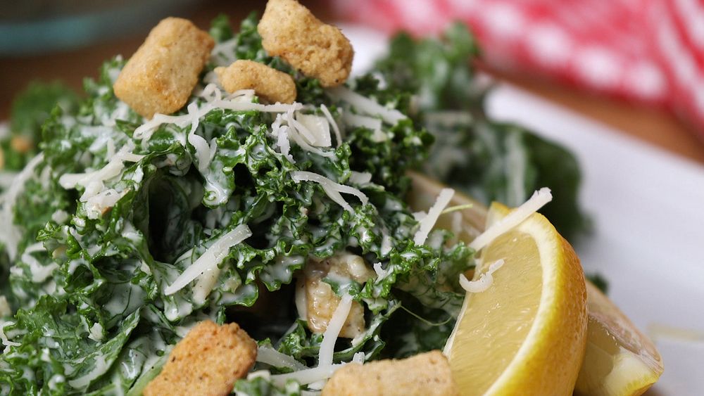 Close up of a creamy Caesar salad with grated cheese, croutons and lemon wedges.