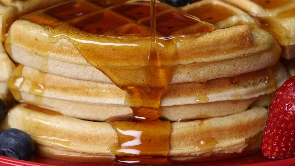 Close up of maple syrup being poured over a stack of waffles.