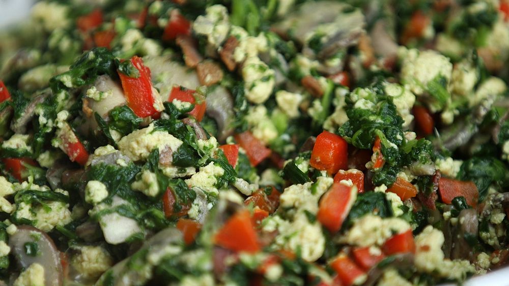 Close up of a spinach egg salad with red peppers, bacon, and mushrooms.
