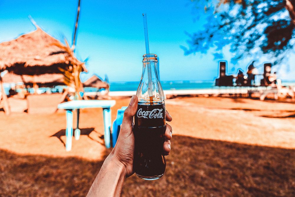 Coke bottle with a straw on a tropical beach blue, location unknown, date unknown