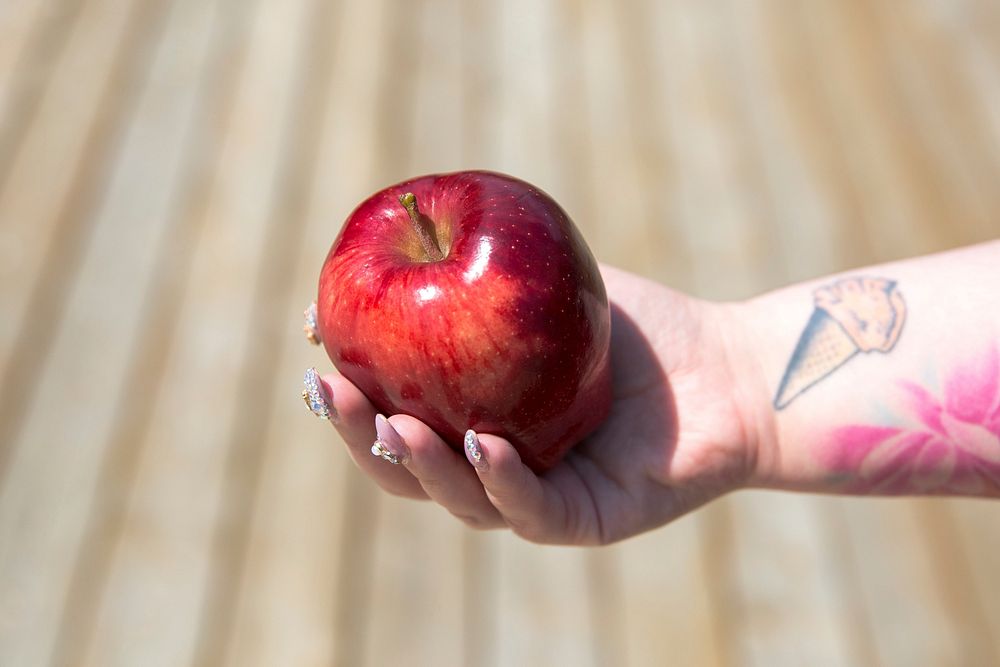 Free woman with tattoos and decorated fingernails holding a red apple in her hand, public domain fruit CC0 photo.