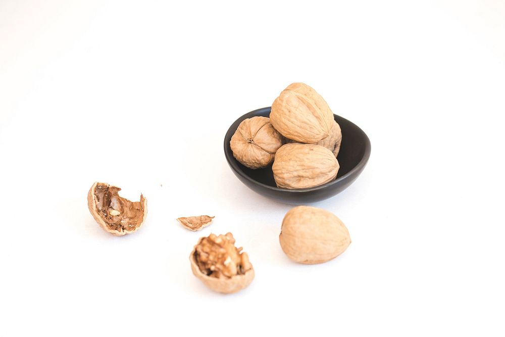 Free cracked walnut beside a dish of whole walnuts image, public domain CC0 photo.