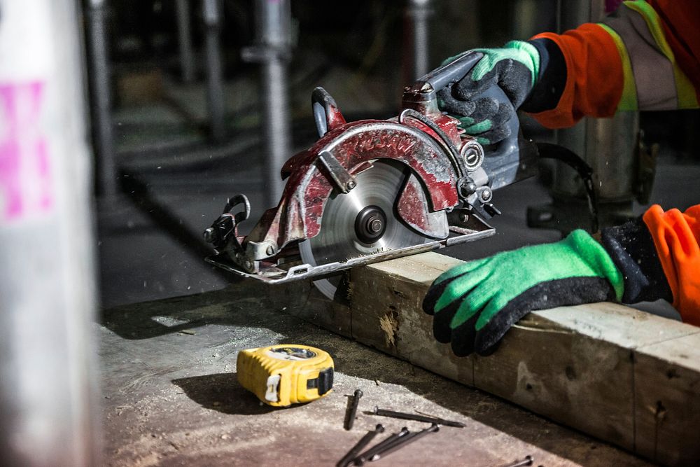 Free construction worker uses a circular saw to cut a wood beam on a construction site photo, public domain CC0 image.