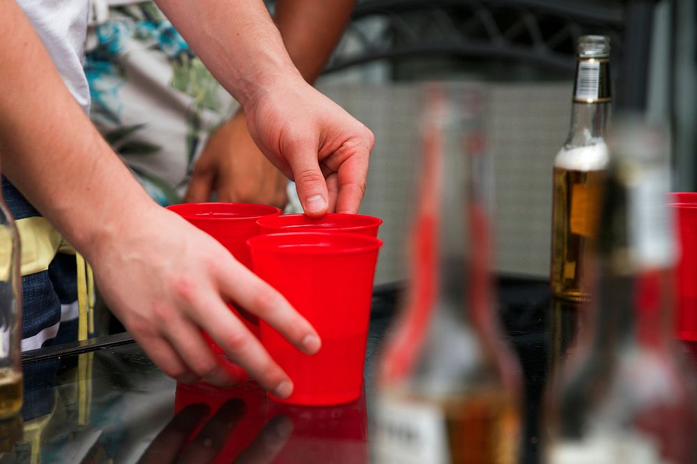 Someone sets up red plactic cups on a table with beer in the background.