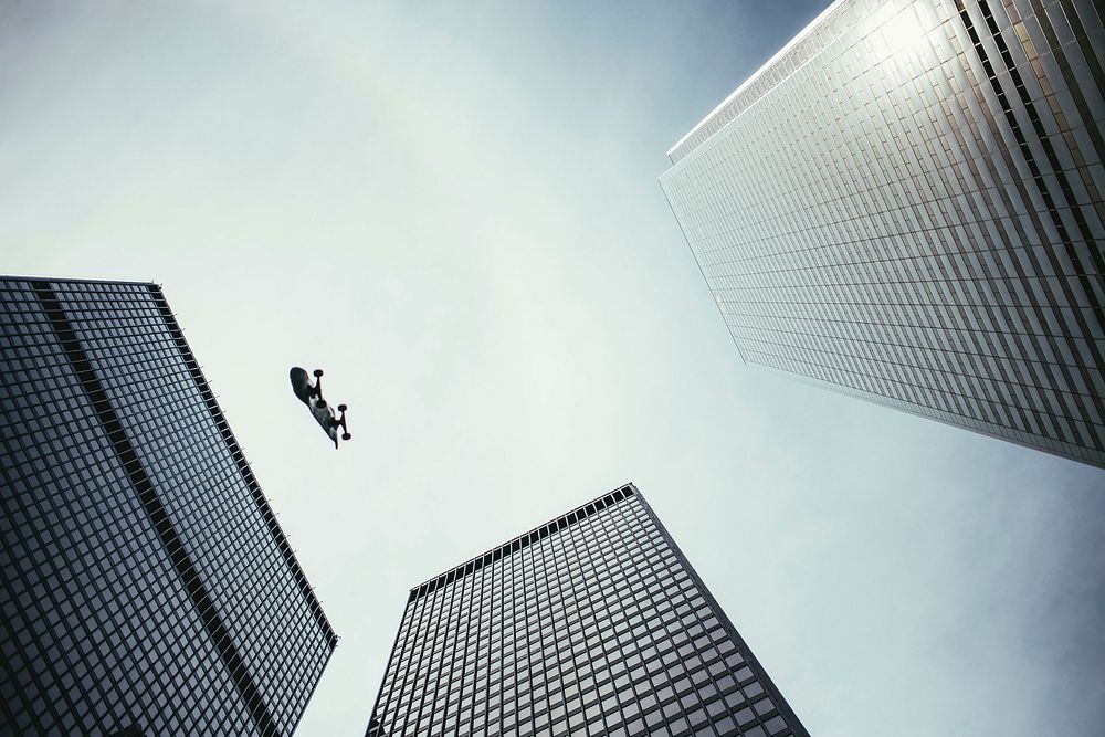 A skateboard falls in the sky between tall city skyscrapers, free public domain CC0 photo.