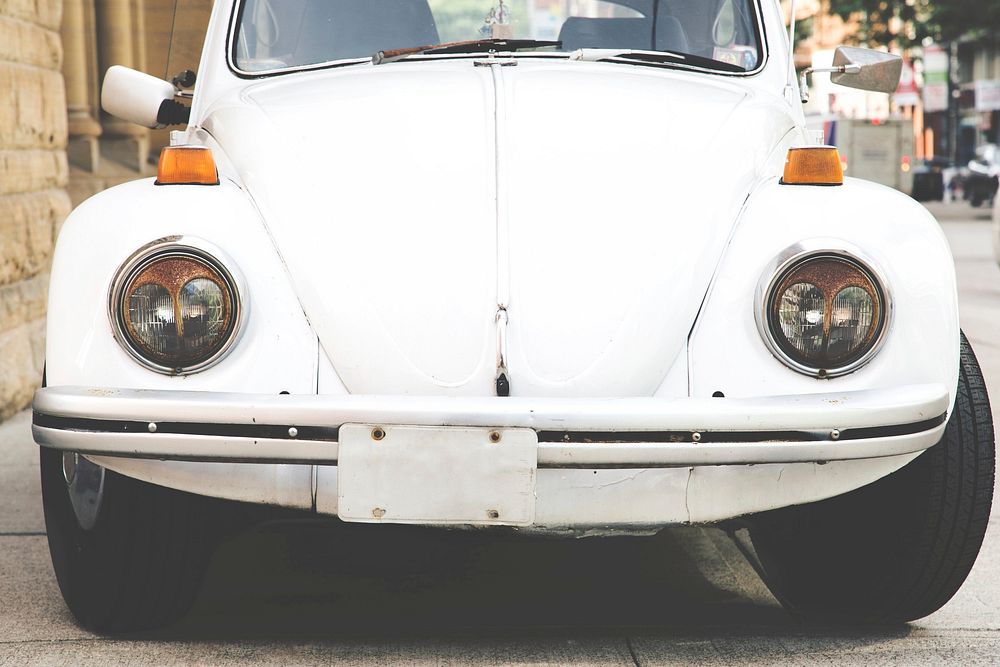 An image facing the front of a white bug shaped car parked in the street. White punch buggy no returnies.