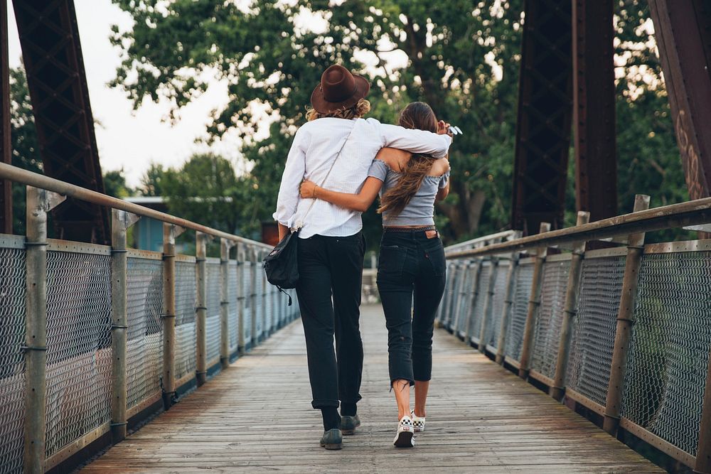 Free young couple walking away on a bridge arm in arm image, public domain CC0 photo.