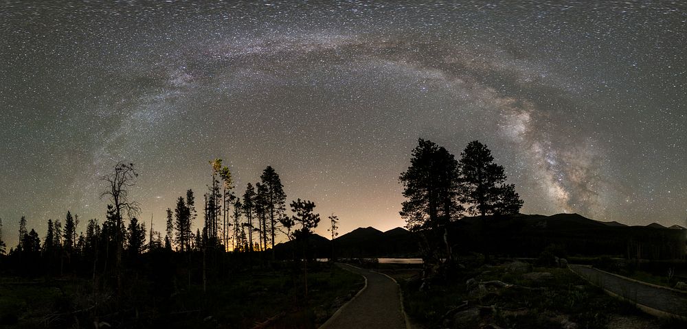 Trees in silhouette against a starry night sky frame this view of the Milky Way at Rocky Mountain National Park, Colorado.…
