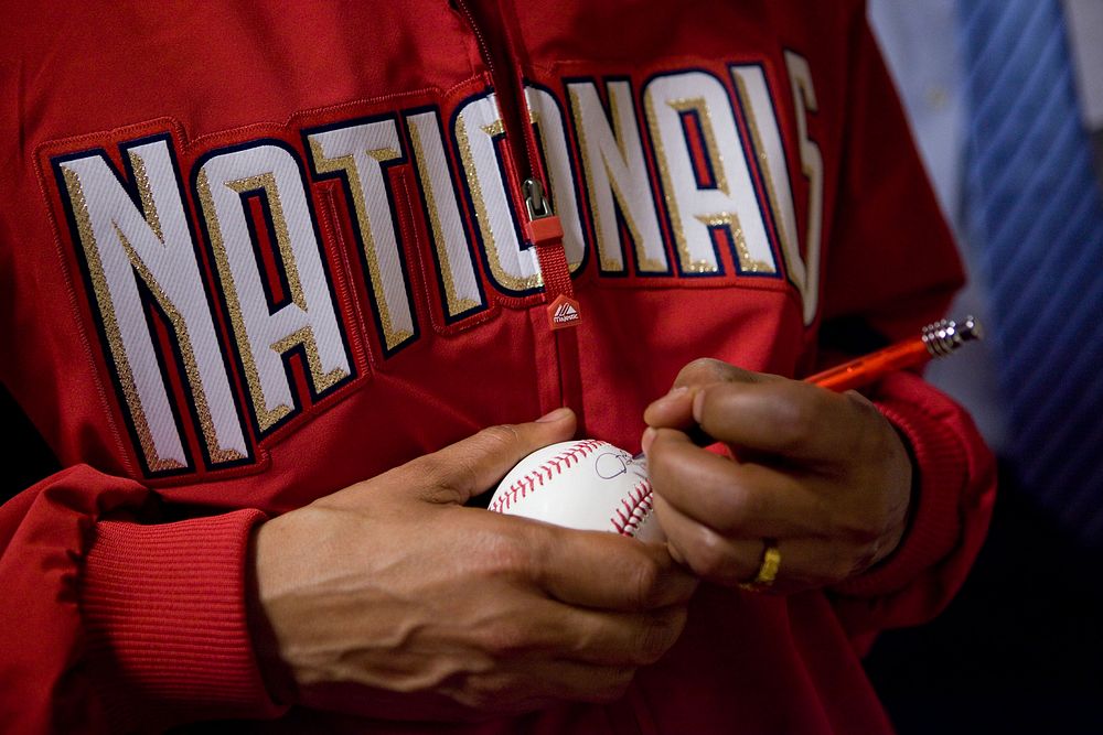 President Barack Obama signs a baseball after throwing out the ceremonial first pitch on opening day of baseball season at…