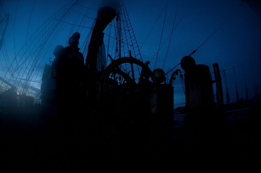 A crew member of the U.S. Coast Guard Cutter Eagle stands helmsman watch as the sun sets Thursday, Sept. 22, 2011. Eagle…