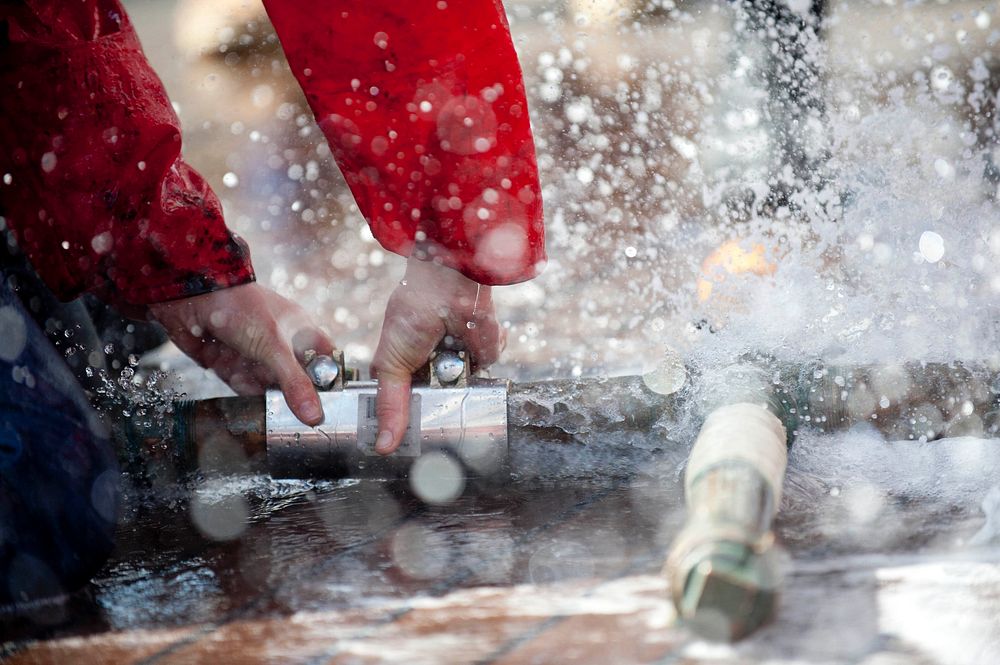 Repairing pipe with hand shots, water splashing. Original public domain image from Flickr