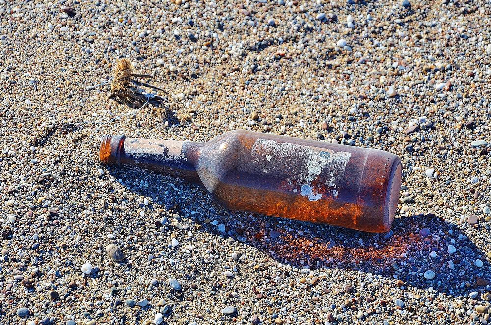 Alcohol bottle on beach sand. Free public domain CC0 image.