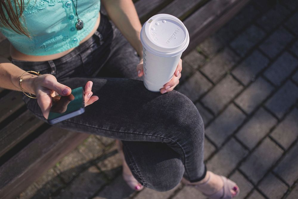 Free woman holding plastic coffee cup and mobile phone public domain CC0 photo.