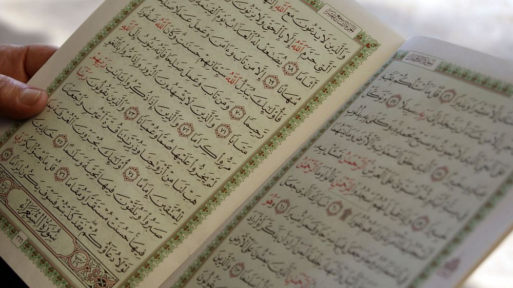 Close up of hand holding a holy quran with open pages. Free public domain CC0 photo.