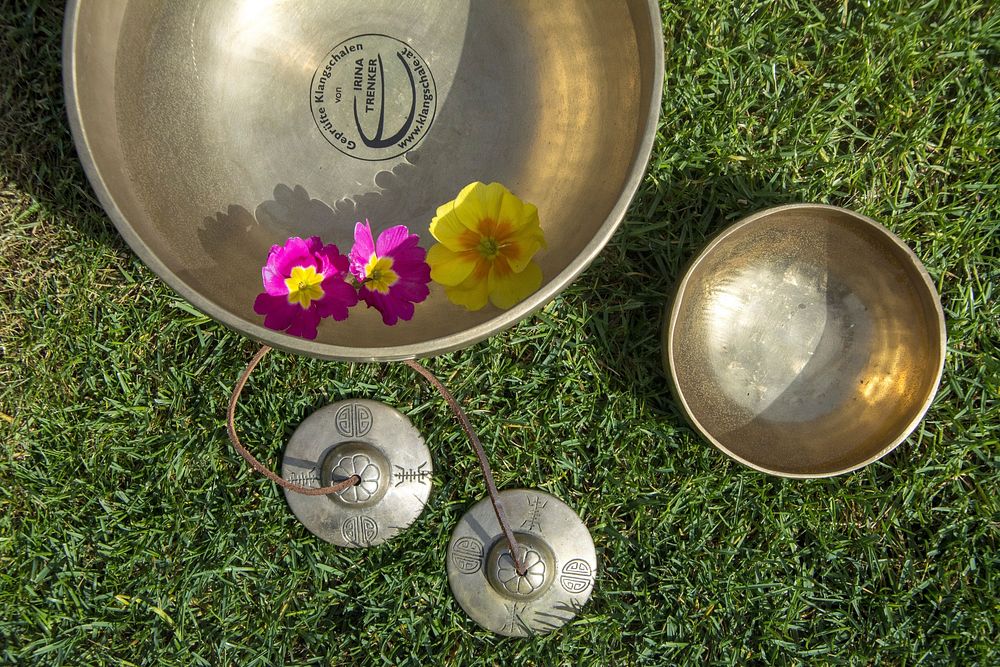 Overhead view of Tibetan singing bowls with flowers on green grass. Free public domain CC0 photo.
