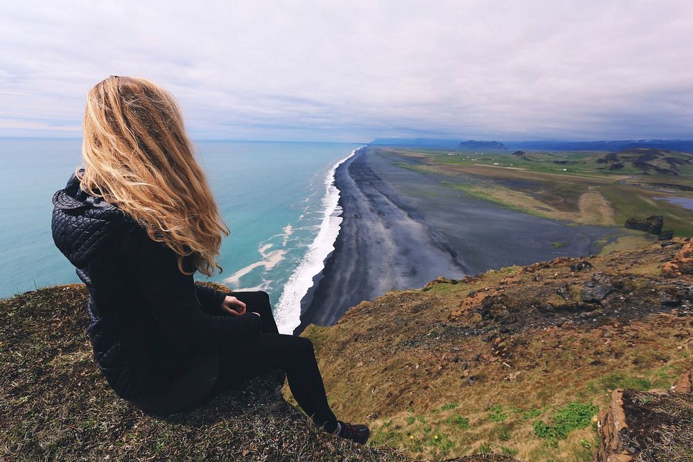 Free woman sitting on cliffs overlooking sea and shoreline public domain CC0 photo.