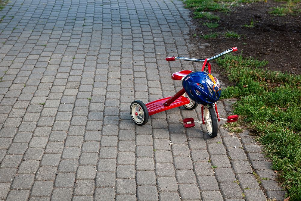 Close up of child tricycle with helmet on the path in the park, free public domain CC0 image.