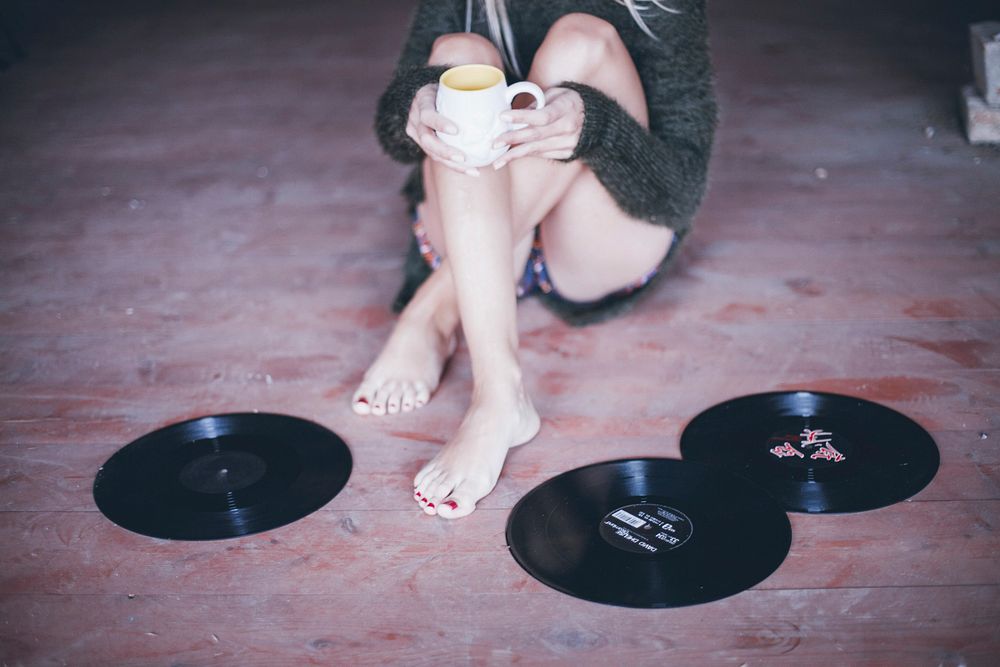 A woman holding a cup of coffee alongside vinyl records on floor