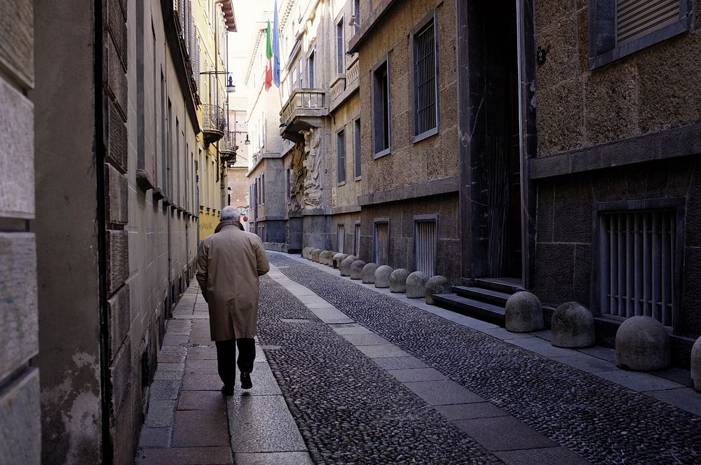 Man walking on pathway between buildings. Free public domain CC0 image.