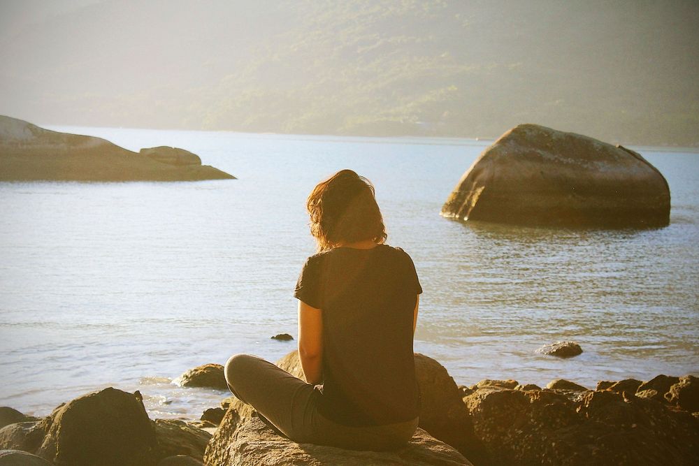 Woman sitting on the rock facing the sea, free public domain CC0 photo/image.