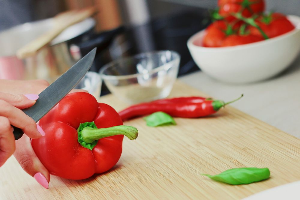 Free woman slicing red bell pepper on chopping board photo, public domain vegetables CC0 image.