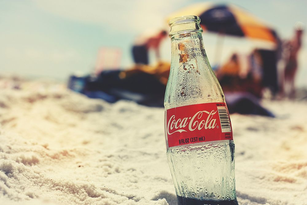 Empty coke glass bottle in sand on beach, location unknown, 15 February 2017. View public domain image source here