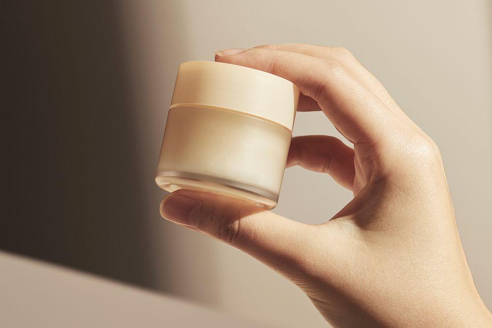 Hand holding beige cosmetic jar, beauty product design
