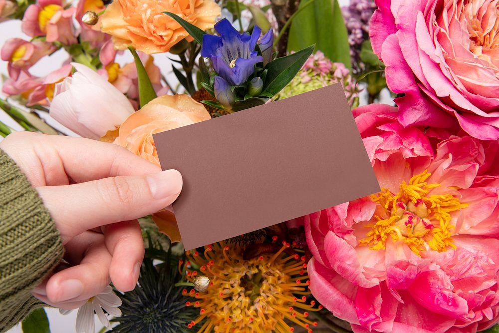 Hand holding blank brown card, flower bouquet background