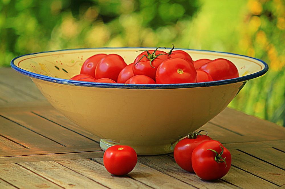 Fresh tomatoes in a big bowl on a wooden table.