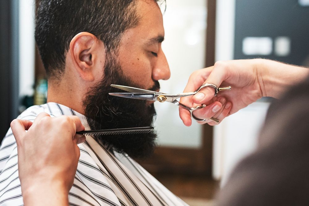 Customer getting a beard trim in a barber shop, small business