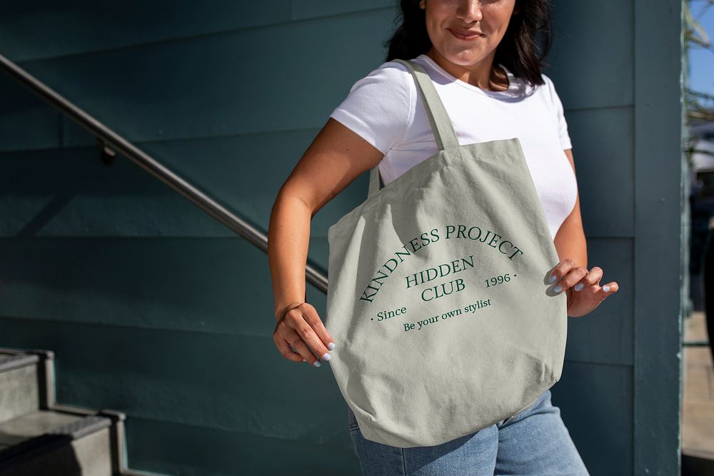 Woman showing a tote bag, green design with text kindness project