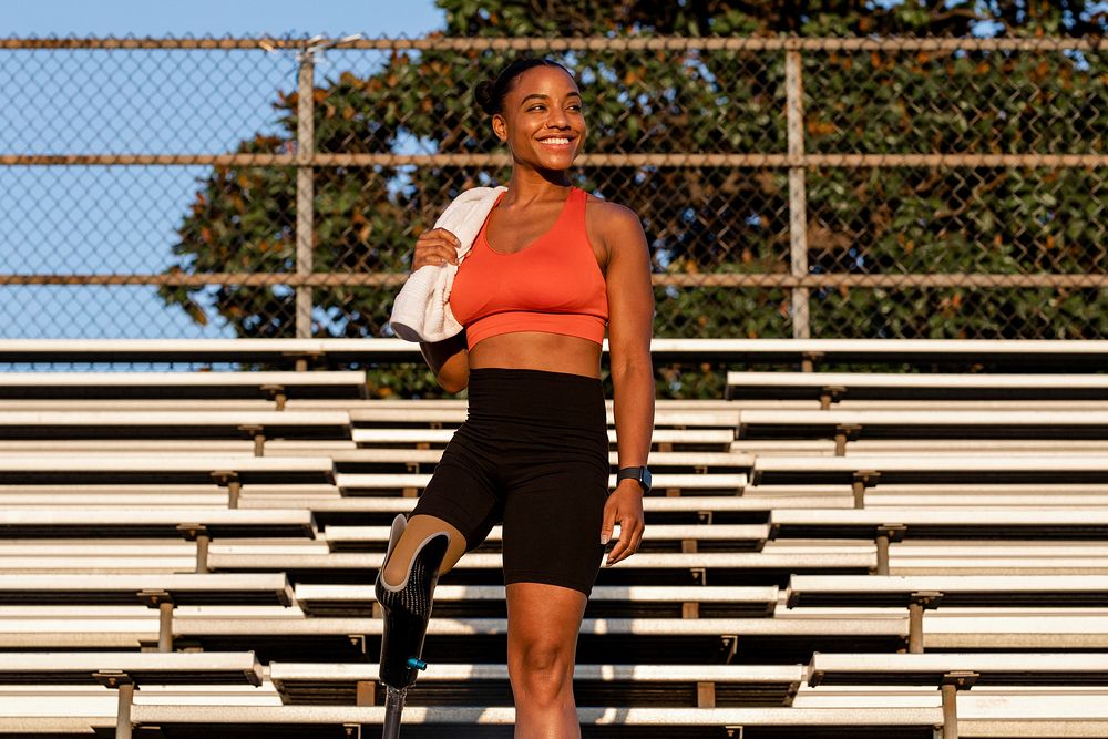 Woman athlete with prosthetic leg smiling carrying a towel standing