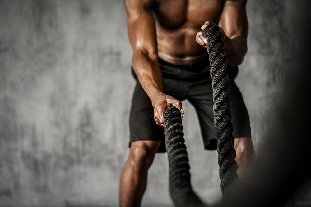 Muscular man working out on the battle ropes in a gym