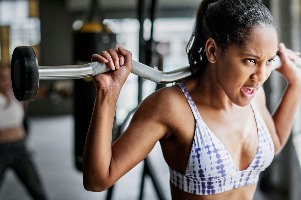 Woman exercising weighlifting with barbell at fitness gym