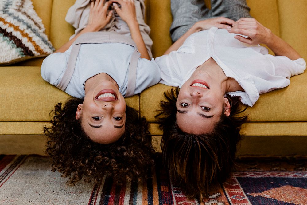 Cheerful women lying upside down on a mustard yellow couch