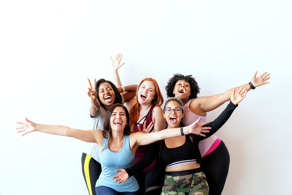 Group of happy sportive women with a white wall