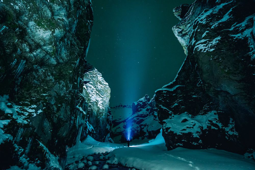 A blue spotlight put onto the starlit sky at the bottom of rock formations in Stakkholtsgjá, Iceland. Original public domain…