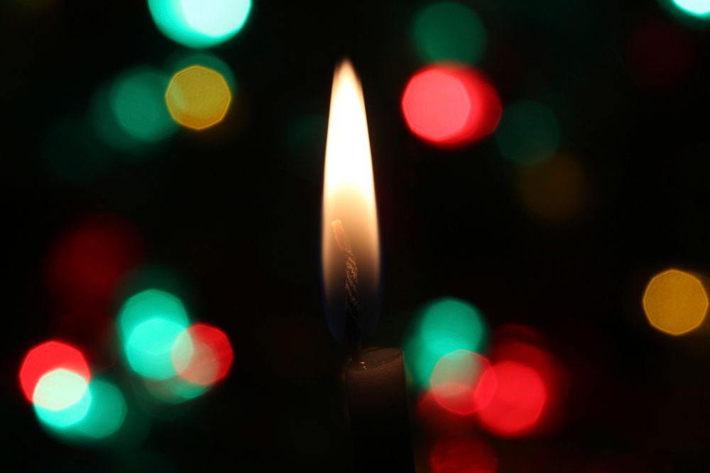 A candle flame burns between a bokeh of festive Christmas lights. Original public domain image from Wikimedia Commons