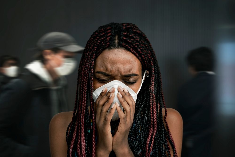 Black woman wearing a mask and coughing in a crowded