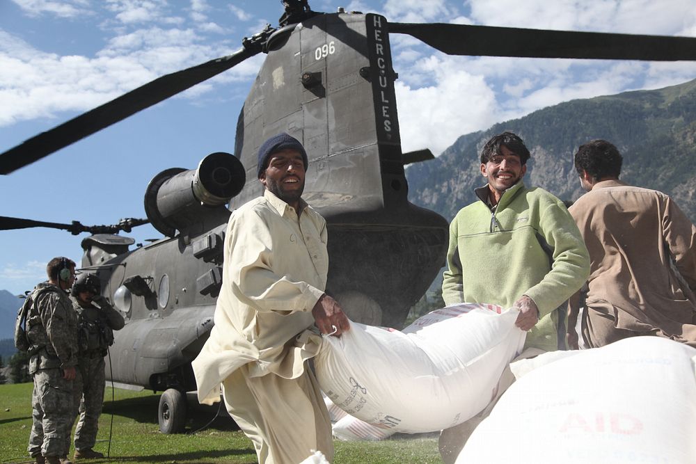 Pakistani men throw a bag of flour onto a pile behind a U.S. Army CH-47 Chinook helicopter that arrived to deliver…