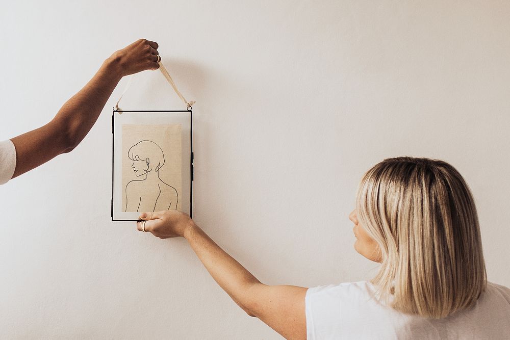 Women hanging aesthetic artwork on white wall