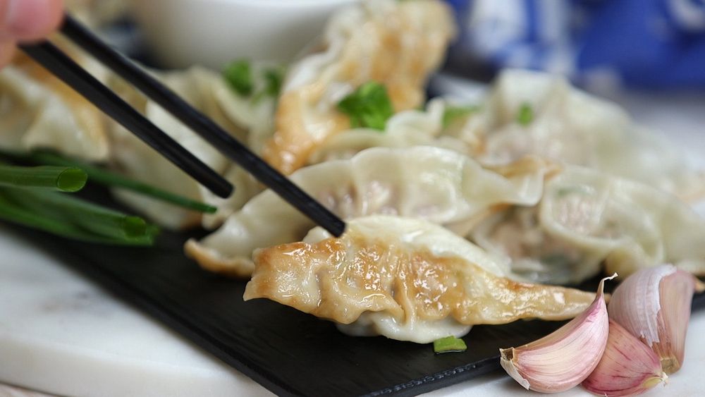 Close up of chopsticks grabbing for a dumpling on a black plate next to garlic.