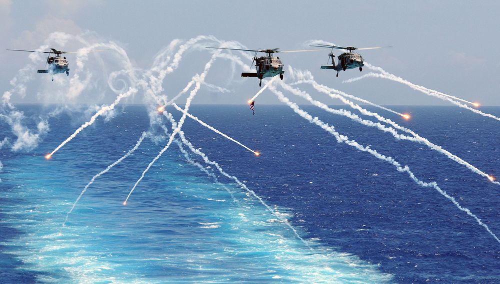 U.S. Navy MH-60S Seahawk helicopters assigned to Helicopter Sea Combat Squadron (HSC) 12 fire flares alongside the aircraft…