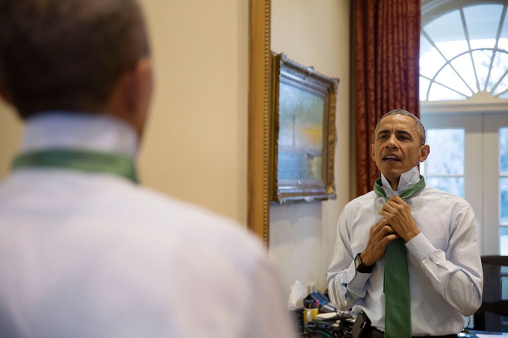 President Barack Obama puts on a green tie in observance of St. Patrick's Day, in the Outer Oval Office, March 17, 2015.