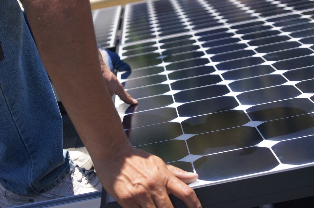 Solar installer lays a module on a California rooftop. Original public domain image from Flickr