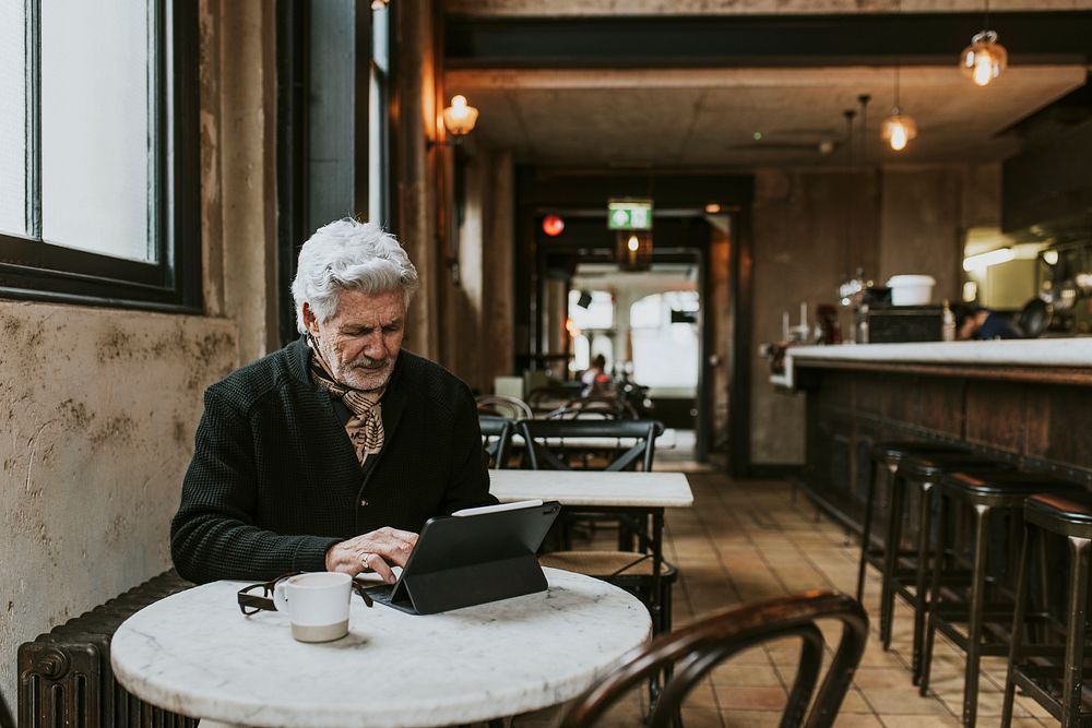 Senior man in video call on digital tablet at cafe