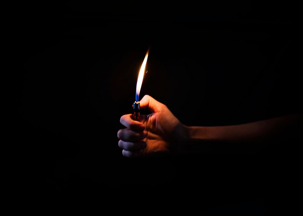 Hand holding lit lighter in the dark